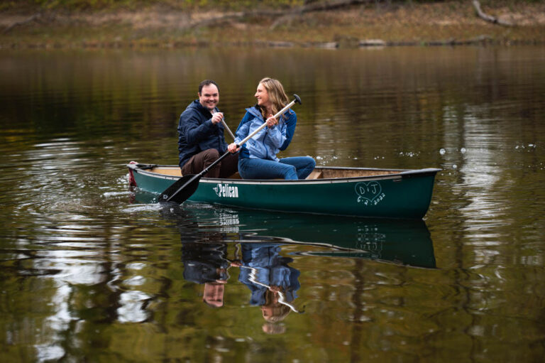 a couple taking engagement photos in a lake they are both sitting in a rowboat together and laughing